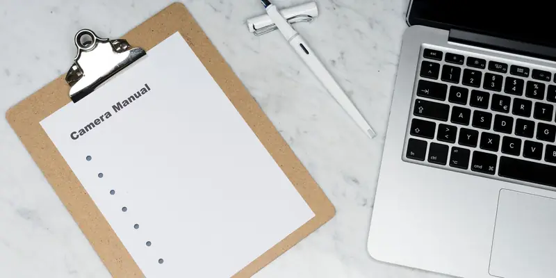 Clipboard with a blank checklist next to a pen and an open laptop on a marble desk